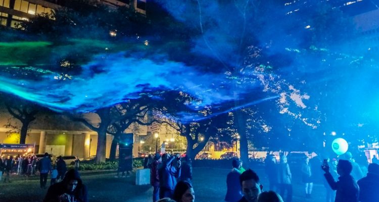 People gathered in a courtyard at night under a blue projection.