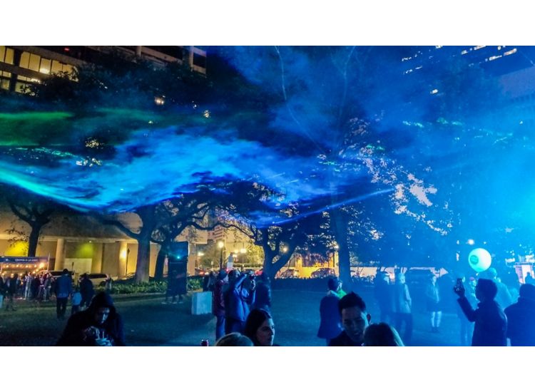 People gathered in a courtyard at night under a blue projection.