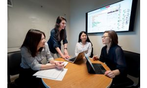 Four women talk in front of screen