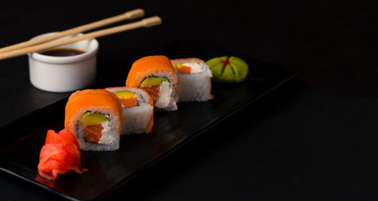 Image of several pieces of sushi on a table next to a container of sauce and chopstick