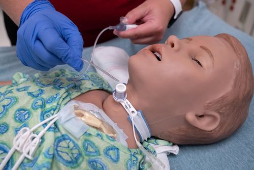 Una enfermera practica el uso de tubos de traqueotomía en un maniquí de niño