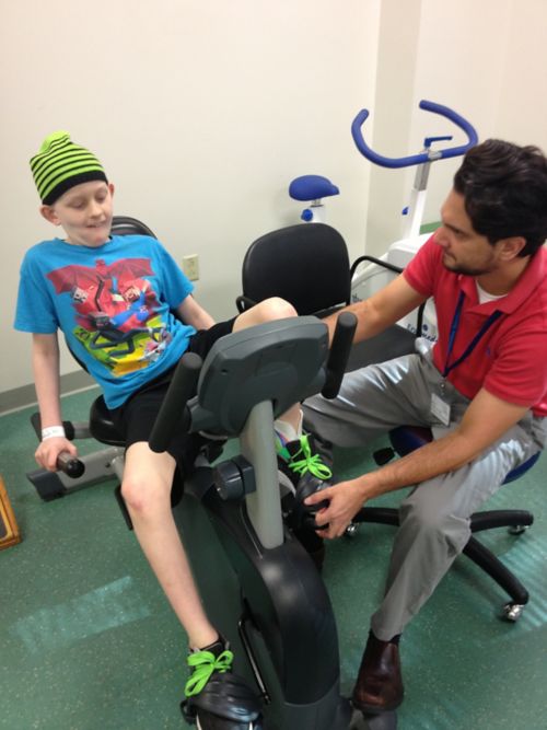 Micah undergoes physical therapy on stationery bike with physical therapist