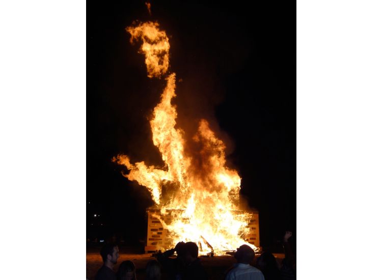 People looking at a large bonfire at night.