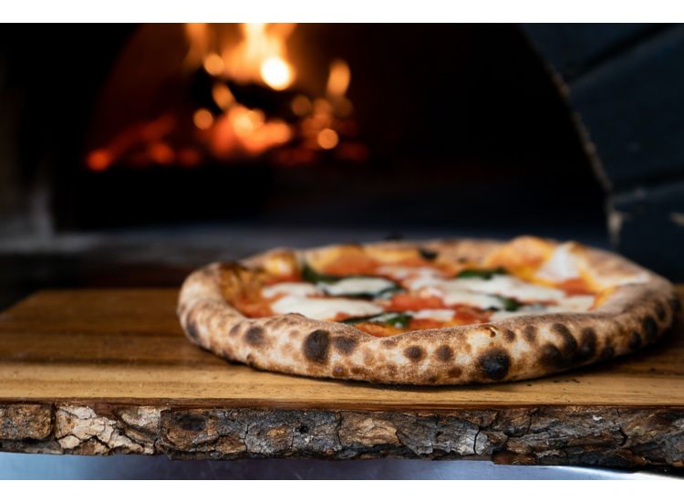 Closeup of ovenfired pizza on a tray in front of the oven.