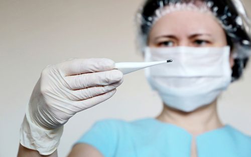 Woman in medical mask measures body temperature