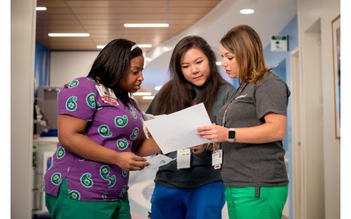 Three female nurses reviewing patient chart in hallway of medical setting