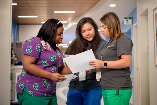 Three nurses stand together in a hallway reviewed a pediatric cancer patient's chart.