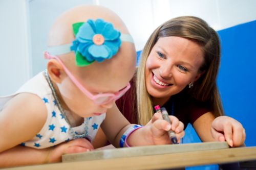 Occupational therapist smiles while working with very young pediatric cancer patient.