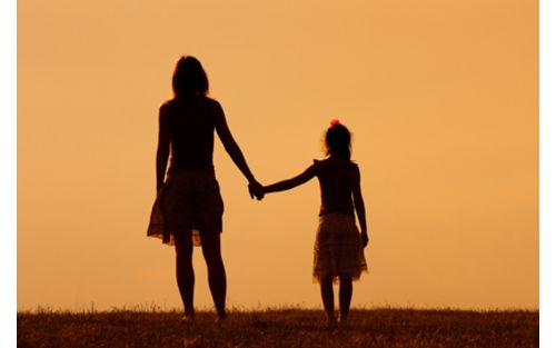 Mother holds hands with young daughter in silhouette.