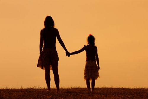 Mother and daughter holding hands in silhouette.
