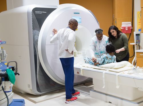 Patient positioned for MRI of her leg with Child Life specialist and two MRI technologists.