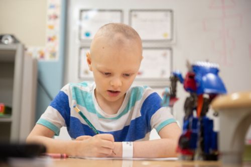 Make a plan for school early in treatment and re-evaluate it regularly. In this photo, a young cancer patient sits at a table working through school assignments.