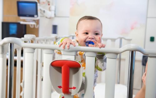 Smiling child standing up in a crib holding onto the railing.