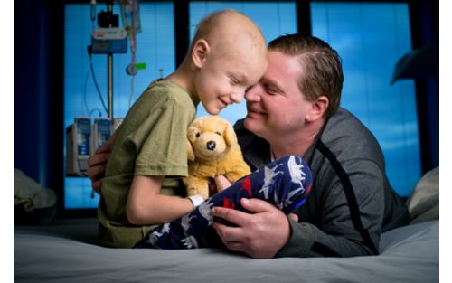 Male child cancer patient talking to father in hospital room