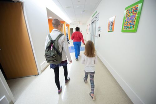 Transitioning off childhood cancer treatment can be a period of uncertainty and anxiety for survivors. In this image, a childhood cancer survivor walks down a hospital hallway behind hospital staff.