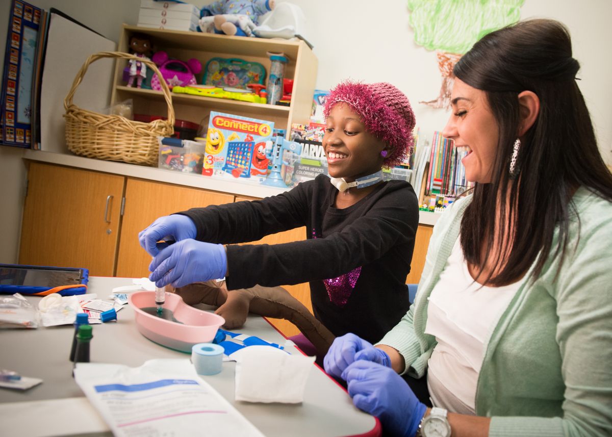  A young girl with cancer is participating in art therapy with a therapist.