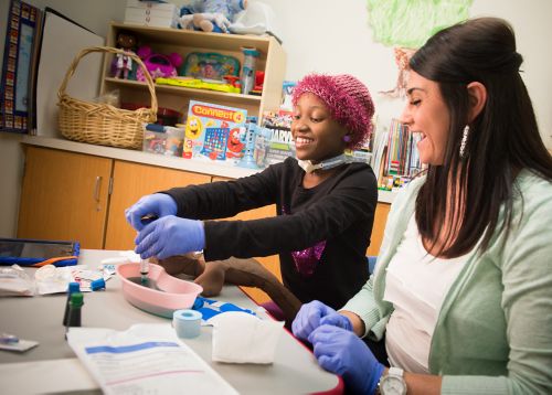 Una joven paciente con cáncer pediátrico prepara una jeringa para pintar con colorantes para alimentos, acompañada por una miembro del personal del hospital.