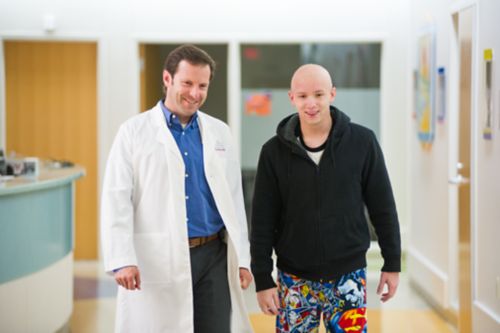 Un patient adolescent atteint d'un cancer pédiatrique marche accompagné d'un médecin dans un couloir