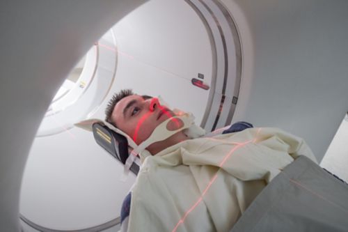 Young male cancer patient is beginning PET scan, red lights visible on his face.