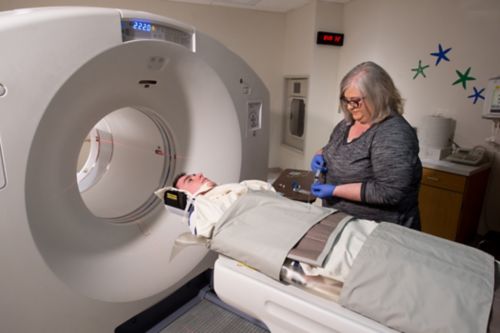 Young male cancer patient receives radioactive tracer while in position for PET scan.