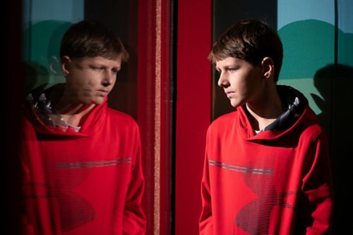 A patient in a red hoody looking at his reflection in a window.