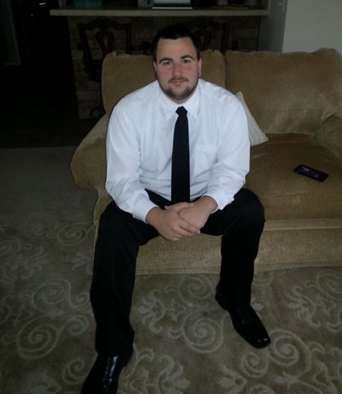 Patient sitting on a couch wearing a white shirt, black tie, and black pants.