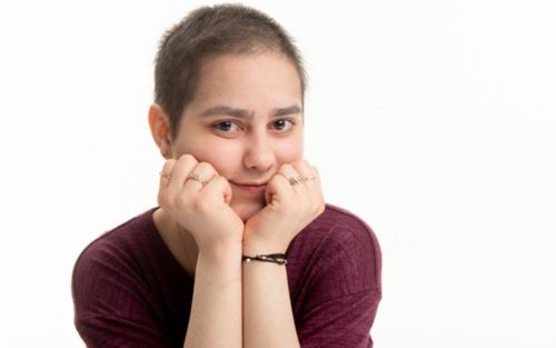 Teenage cancer survivor looking at camera, with her chin resting in her hands