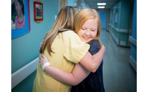 Care team member hugging female pediatric patient