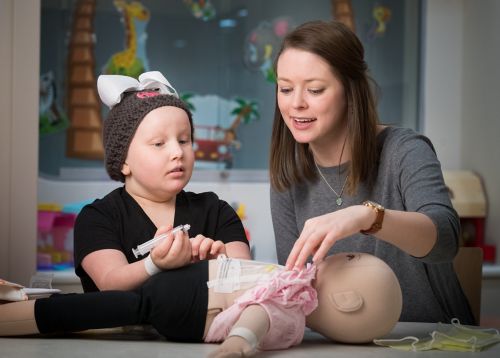 Child Life Specialist engages a young cancer patient in medical play to prepare her for an exam.