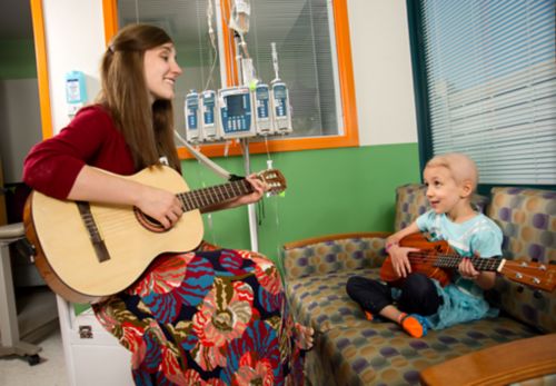 A child cancer patient and music therapist play guitar together.