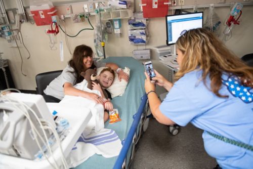 Un niño y su madre posan para una fotografía que toma un miembro del personal de enfermería en la habitación del hospital