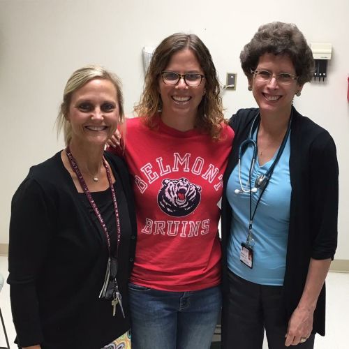 A cancer survivor standing with two members of a care team in an examination room.