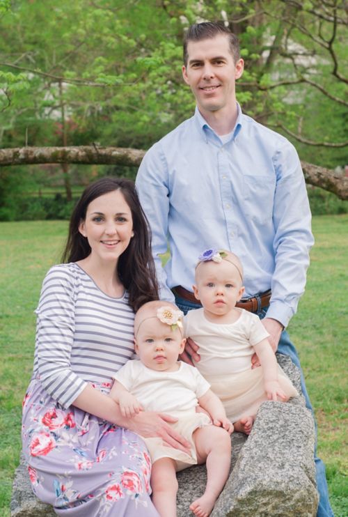 A family gathered outside with two adults and two twin toddlers seated on a rock.