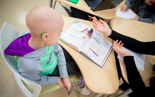 Child cancer patient sitting at school desk with open textbook.