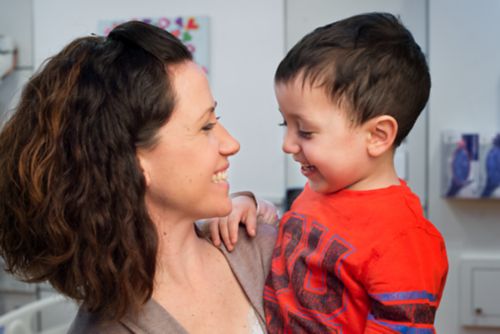 Pediatric cancer patient smiles at his mom while she holds him