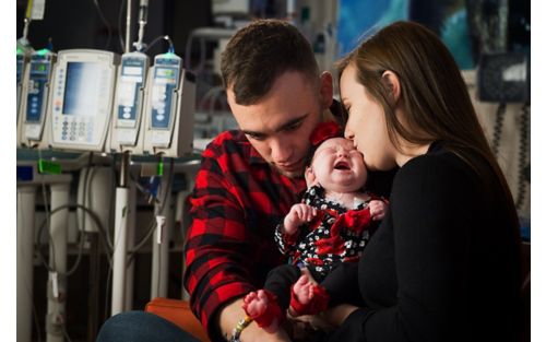 A family comforts a crying infant patient in a hospital room.