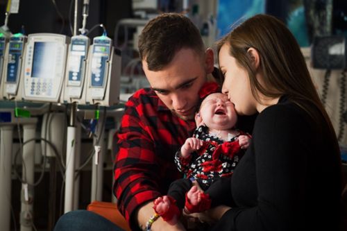 A family comforts a crying infant patient in a hospital room.