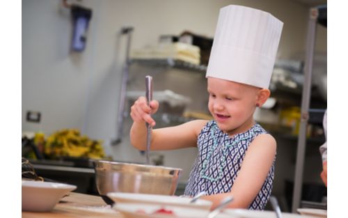 Female child wearing chefs hat in kitchen stirring bowl
