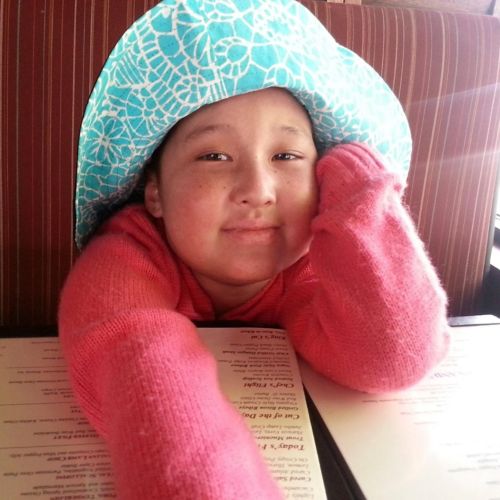 Patient leaning on table wearing a pink sweater and blue hat