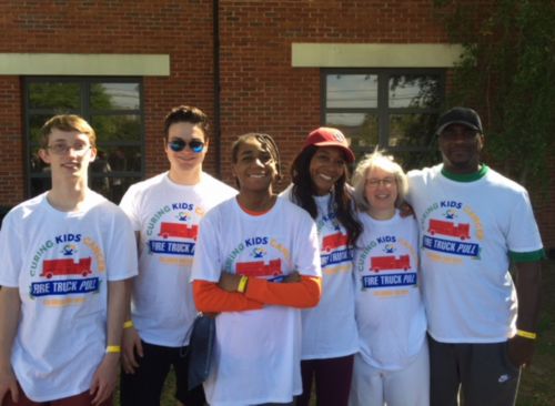 A group of people wearing matching white shirts standing in front of a building at a childhood cancer event.