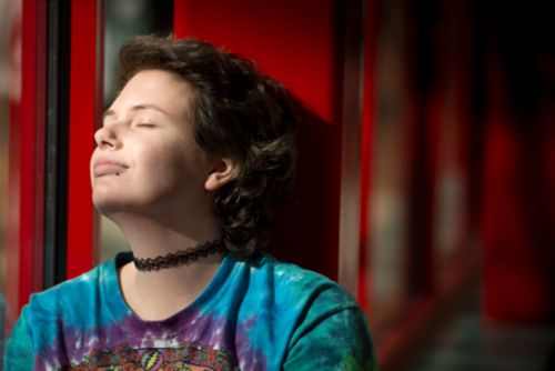 Un adolescent est assis devant une fenêtre avec les yeux fermés et médite.