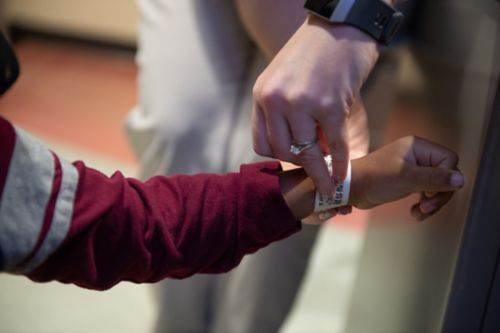 Cuando su hijo tiene cáncer, empacar para una hospitalización puede ser abrumador. La imagen muestra la mano de una empleada encargada de la admisión que le coloca una pulsera de hospital a un paciente de cáncer infantil.