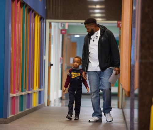 It can be helpful to bring copies of important documents such as your child’s birth certificate, Social Security numbers for the patient and parents or guardians, insurance documents, copies of any custody papers, and other legal papers that pertain to the patient’s health. This photo depicts a father and son walking down a hospital hallway.