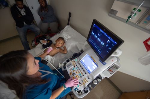 Una enfermera realiza un ecocardiograma a un niño pequeño en una habitación de hospital.