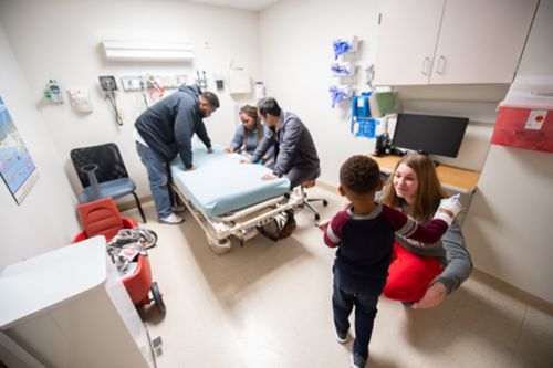 Limite las distracciones para que pueda concentrarse en la información que el equipo de atención comparte con usted. Pídale a alguien que cuide a los niños más pequeños. En esta foto, una enfermera extiende sus brazos para abrazar a un paciente con cáncer infantil mientras los padres hablan con el médico en el fondo.