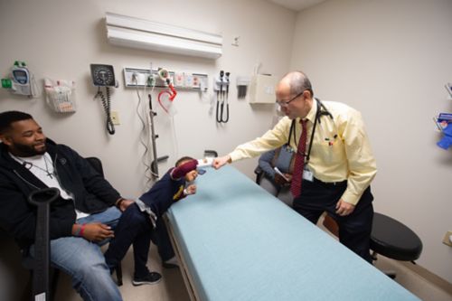Good relationships between families and care team members help build trust and encourage partnership in decision making. In this photo, a younger childhood cancer patient fist bumps with his pediatric oncologist in a clinic room.
