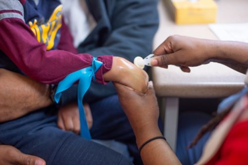 A nurse ties a tourniquet and presses to find the best vein for an IV. The nurse cleans the area where she will place the IV.