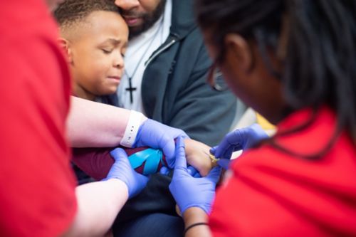 While one staff member stabilizes the patient’s arm, another nurse inserts the needle into the patient’s hand. 