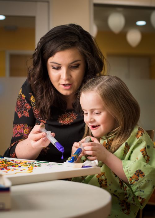 Young pediatric cancer patient paints with syringes accompanied by a member of hospital staff