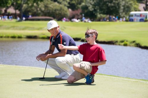 Jeune patient atteint d'un rhabdomyosarcome agenouillé, discutant avec un golfeur à l'occasion d'un tournoi